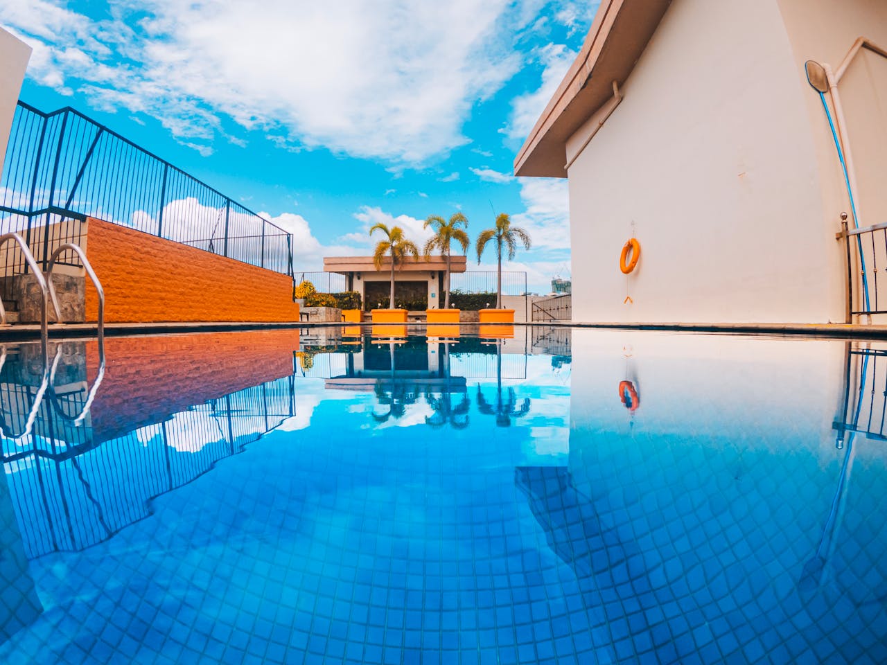 Stunning clear blue swimming pool reflecting palm trees and tropical sky.